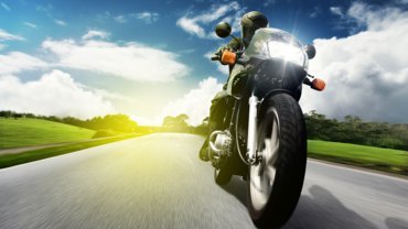 Black Motorcycle on its way on the road with the sun and green grass in the background