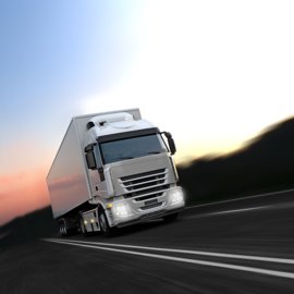 Ein weißer Lastwagen fährt auf der Autobahn mit dem Sonnenuntergang im Hintergrund.