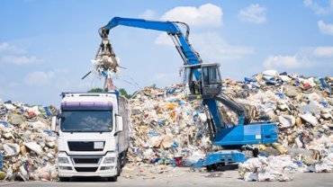 Bild einer Maschine, die Abfälle in einen LKW verlädt, der für Schlemmer Waste Management Industry steht.